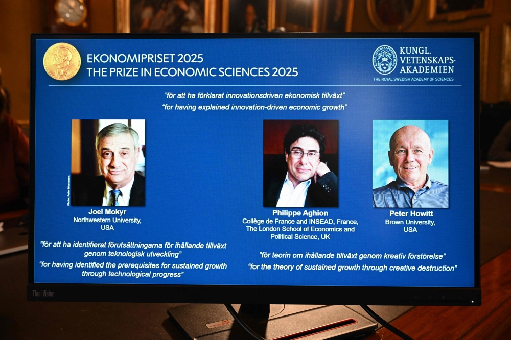 A screen displays the portraits of the 2025 prize winners (L-R) Joel Mokyr, Philippe Aghion and Peter Howitt, during the announcement of the winners of the 2025 Nobel Prize in Economics, the Sveriges Riksbank Prize in Economic Sciences in Memory of Alfred Nobel, at the Royal Swedish Academy of Sciences in Stockholm, Sweden, on October 13, 2025.  (Photo by Jonathan Nackstrand / AFP)