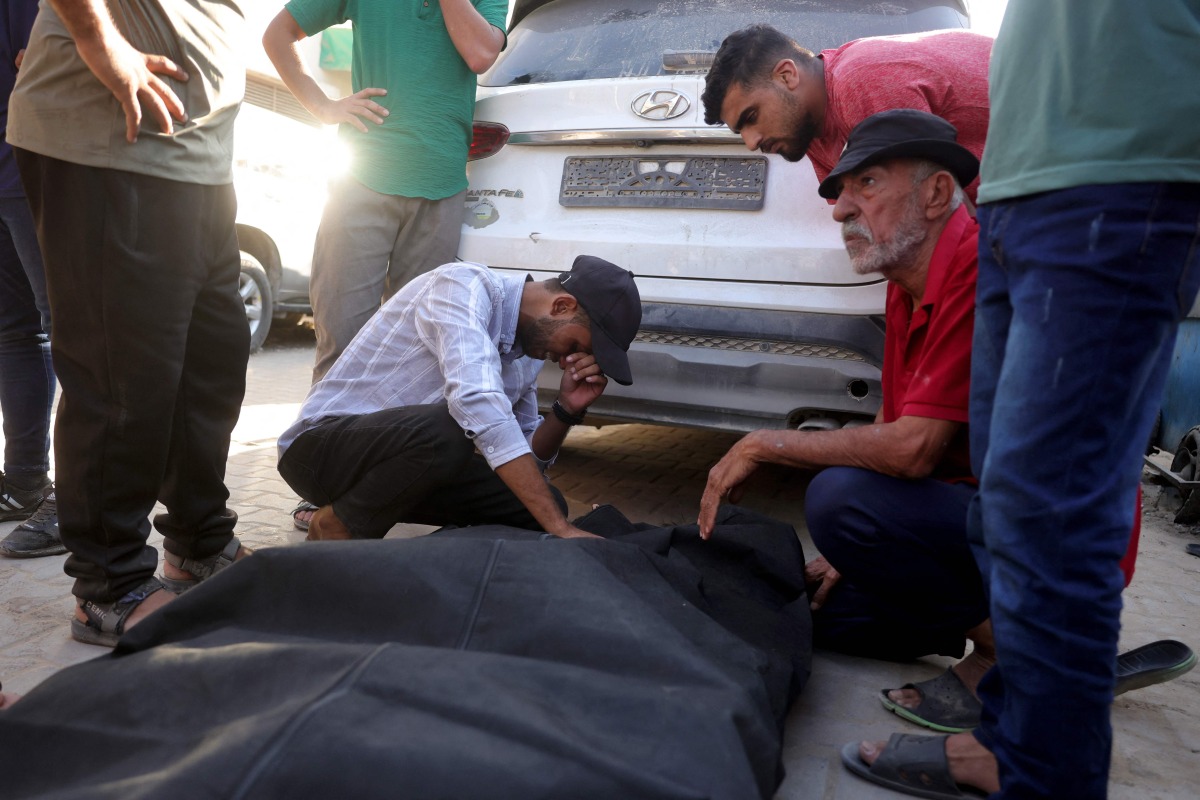 Friends and relatives mourn over the shrouded body of a man killed in an Israeli strike earlier, as he is brought to Deir al-Balah's Shuhada al-Aqsa hospital in the central Gaza Strip on October 19, 2025. (Photo by BASHAR TALEB / AFP)
