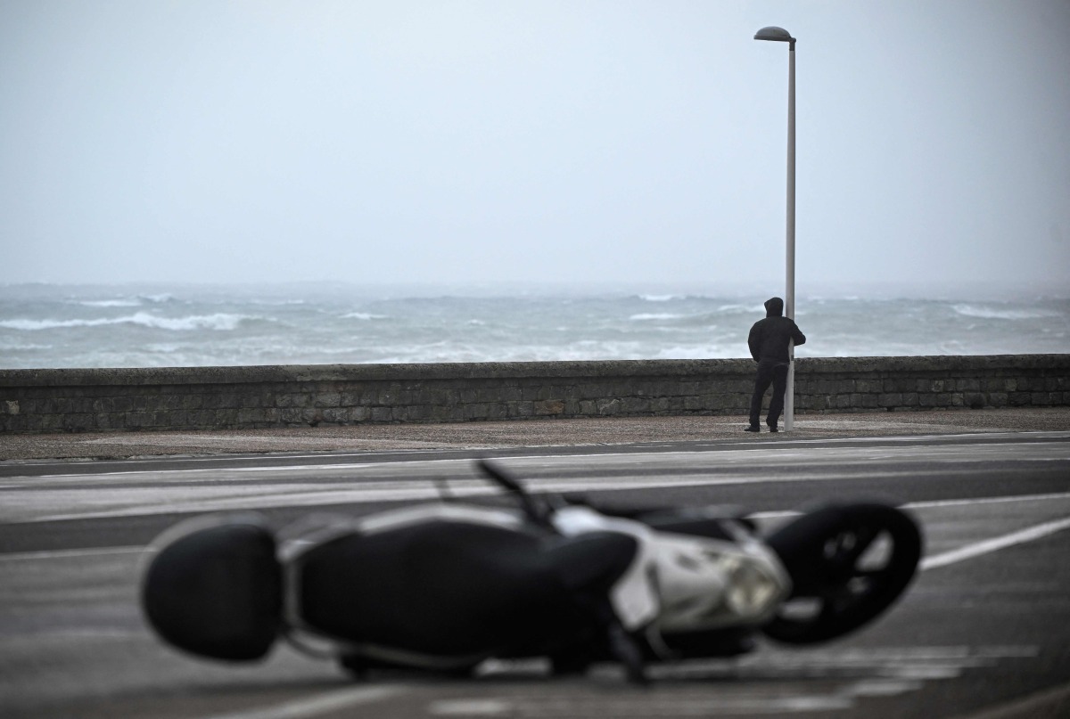 A person holds on to a lamppost as an overturned scooter is seen on a street on October 23, 2025 in San Sebastian, northern Spain, amid strong winds and a rough sea. (Photo by ANDER GILLENEA / AFP)