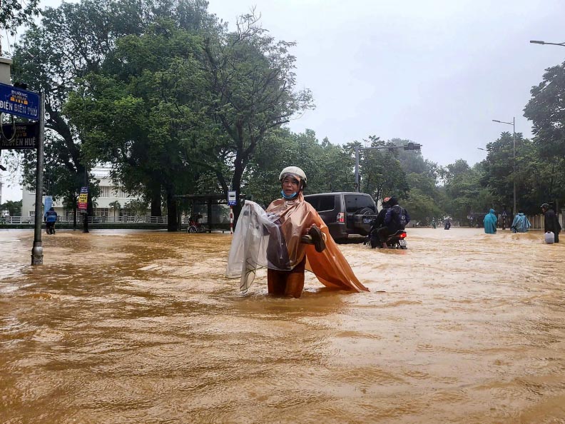 A woman wearing a raincoat wades through a flooded street in Hue on October 28, 2025. Photo by AFP