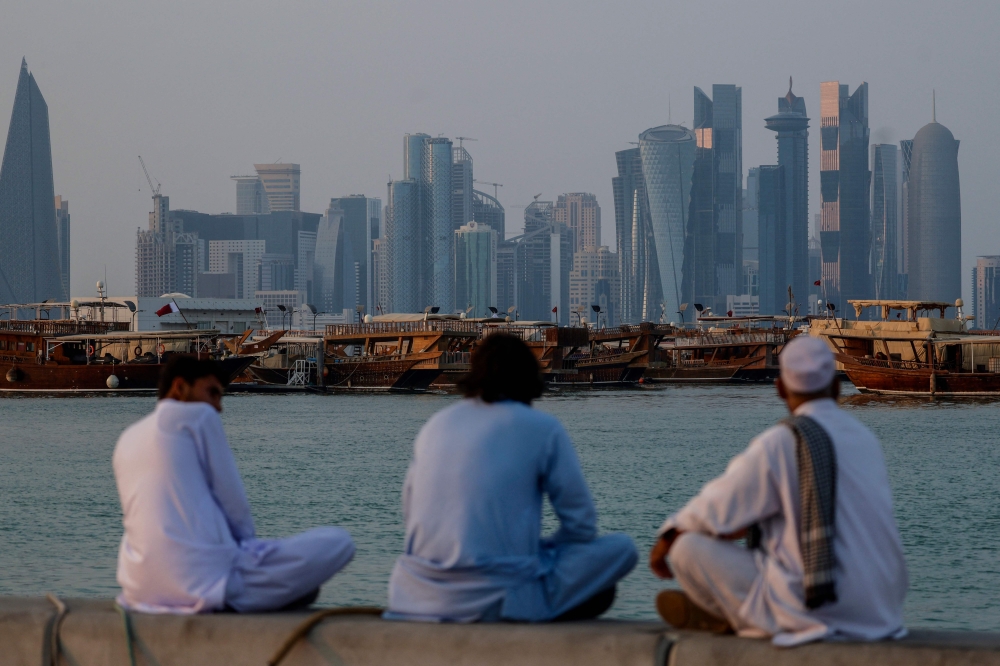 People sit along the corniche facing traditional dhow boats anchored in front of the Doha skyline on October 29, 2025. (Photo by Karim Jaafar / AFP)