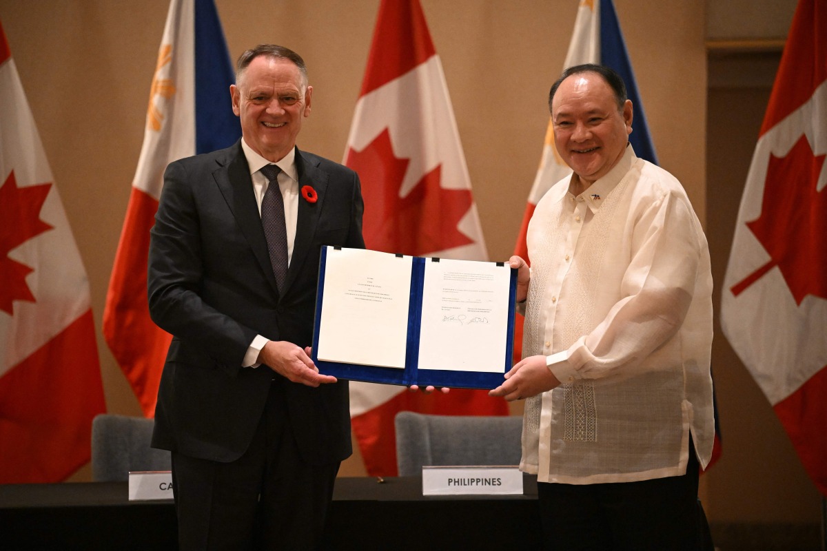 Philippines' Secretary of National Defence Gilberto Teodoro (R) with Canadian Minister of Defence David McGuinty hold their signed documents of the visiting forces agreement after their bilateral meeting in Manila on November 2, 2025. (Photo by Ted ALJIBE / AFP)