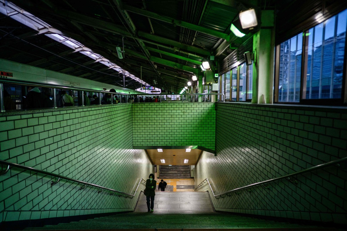 Commuters walk up a staircase towards a platform at a metro station in Seoul on November 4, 2025. (Photo by ANTHONY WALLACE / AFP)