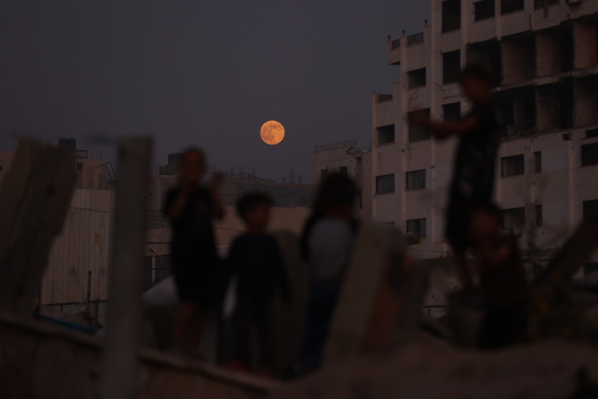 Children play as the moon rises above Gaza City on November 5, 2025. (Photo by Omar AL-QATTAA / AFP)
