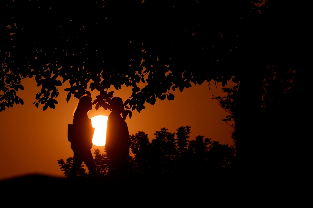 People are silhouetted by the setting sun as they walk in Doha on November 9, 2025. (Photo by Karim Jaafar / AFP)
