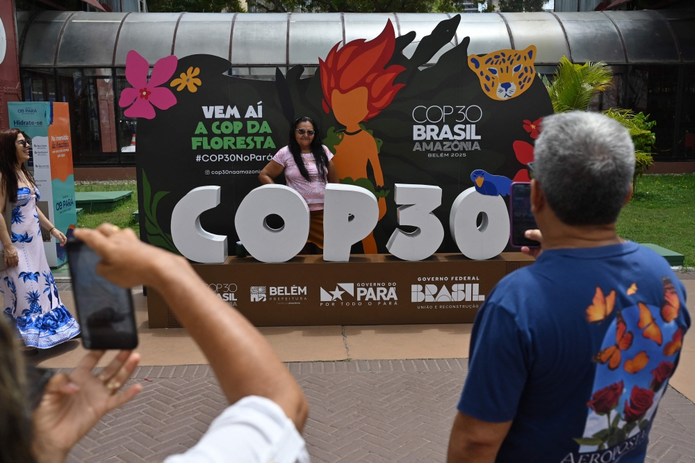 A tourist poses for a picture with COP30 mascot inside the Estacao das Docas, a tourist port area in Belem, Para State, Brazil on November 7, 2025. The COP30 UN Climate Change Conference takes place from November 10 to 21, in Belem, Para state, Brazil. (Photo by MAURO PIMENTEL / AFP)
