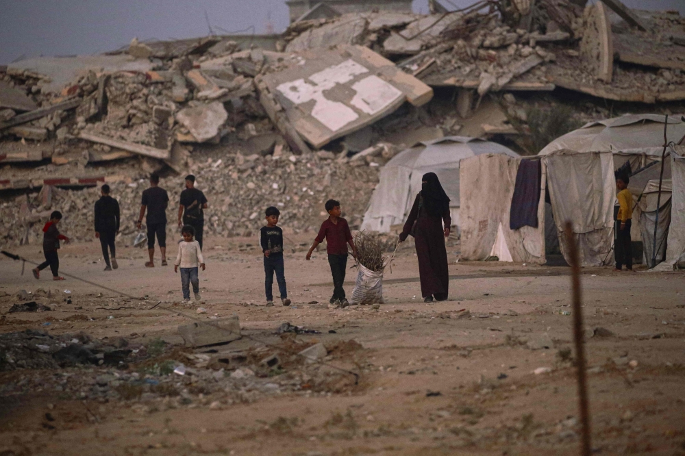 Displaced Palestinians walk past the rubble from buildings destroyed by the Israeli military, in the Bureij refugee camp, in the central Gaza Strip on November 10, 2025. (Photo by Eyad Baba / AFP)