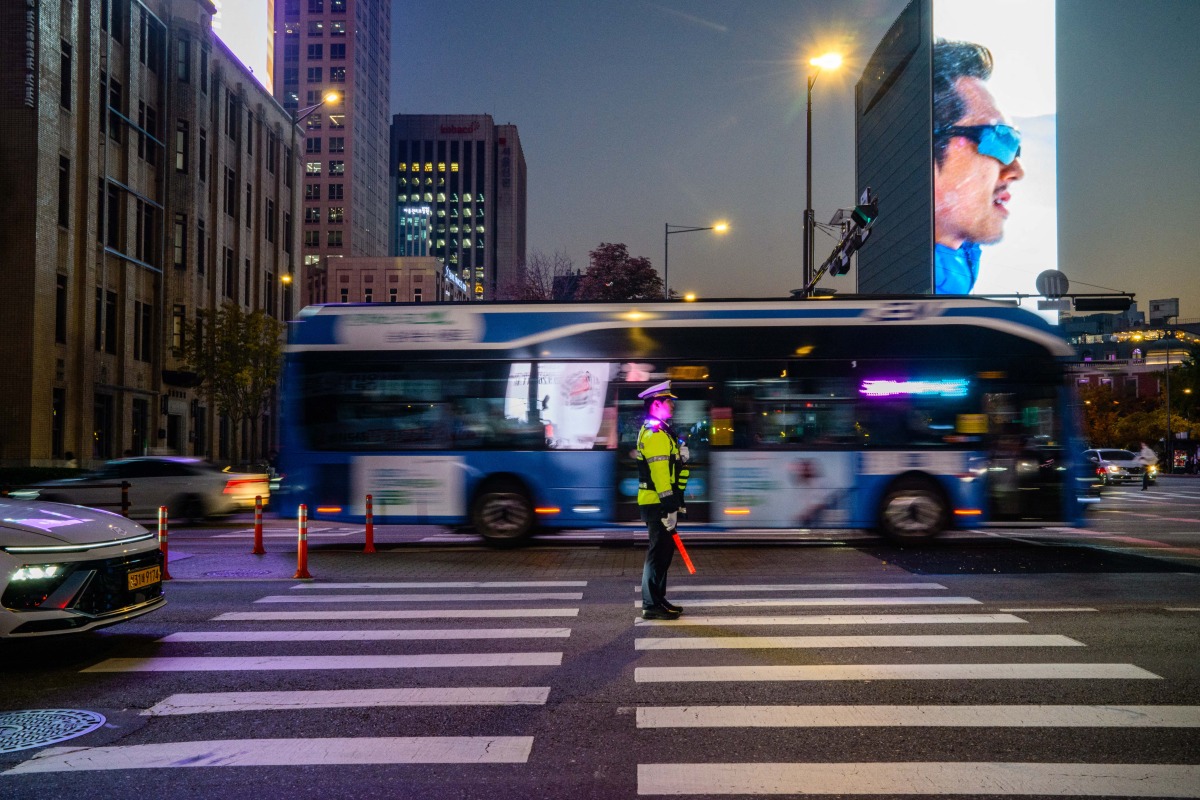 Vehicles drive past a traffic policeman in the Gwanghwamun district of Seoul on November 7, 2025. (Photo by ANTHONY WALLACE / AFP)