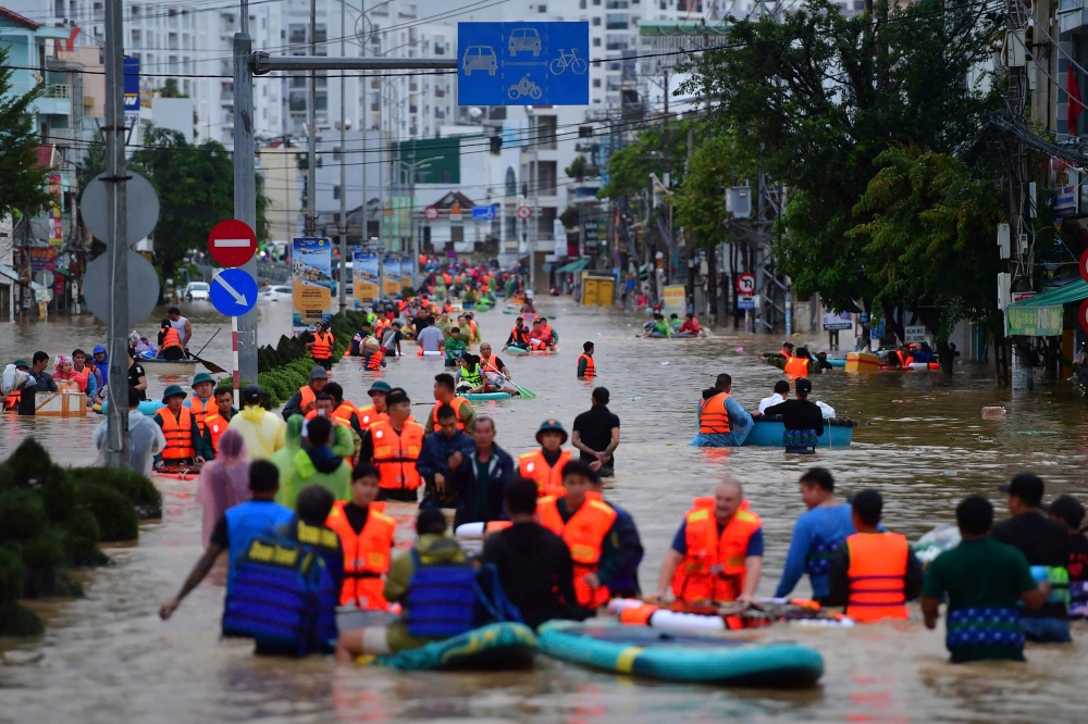 This photo taken on November 20, 2025 shows people wading through floodwaters in Nha Trang in Vietnam's coastal province of Khanh Hoa. (Photo by Duc Thao / AFP)