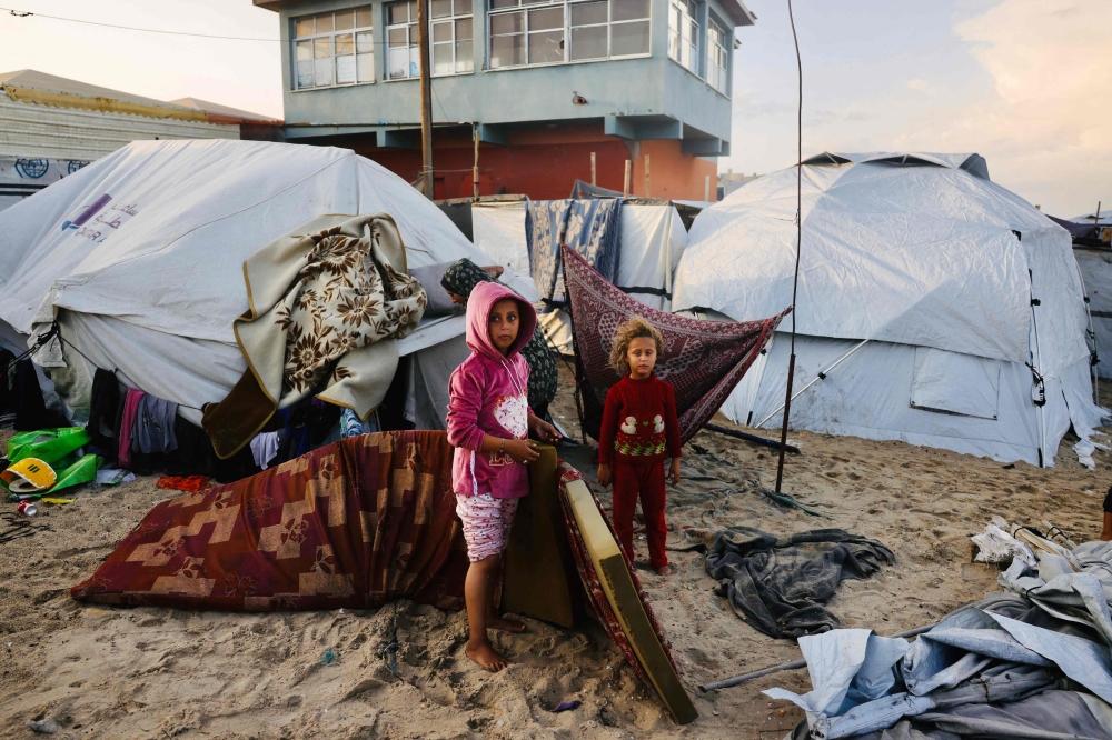 Palestinian children move mattresses to protect them from the rain at a makeshift camp housing displaced Palestinians in Deir al-Balah on November 25, 2025. (Photo by Bashar Taleb / AFP)