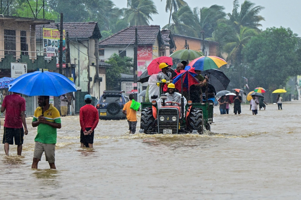 People move through a flooded road after heavy rainfall in Kaduwela on the outskirts of Colombo on November 28, 2025.  (Photo by Ishara S. Kodikara / AFP)