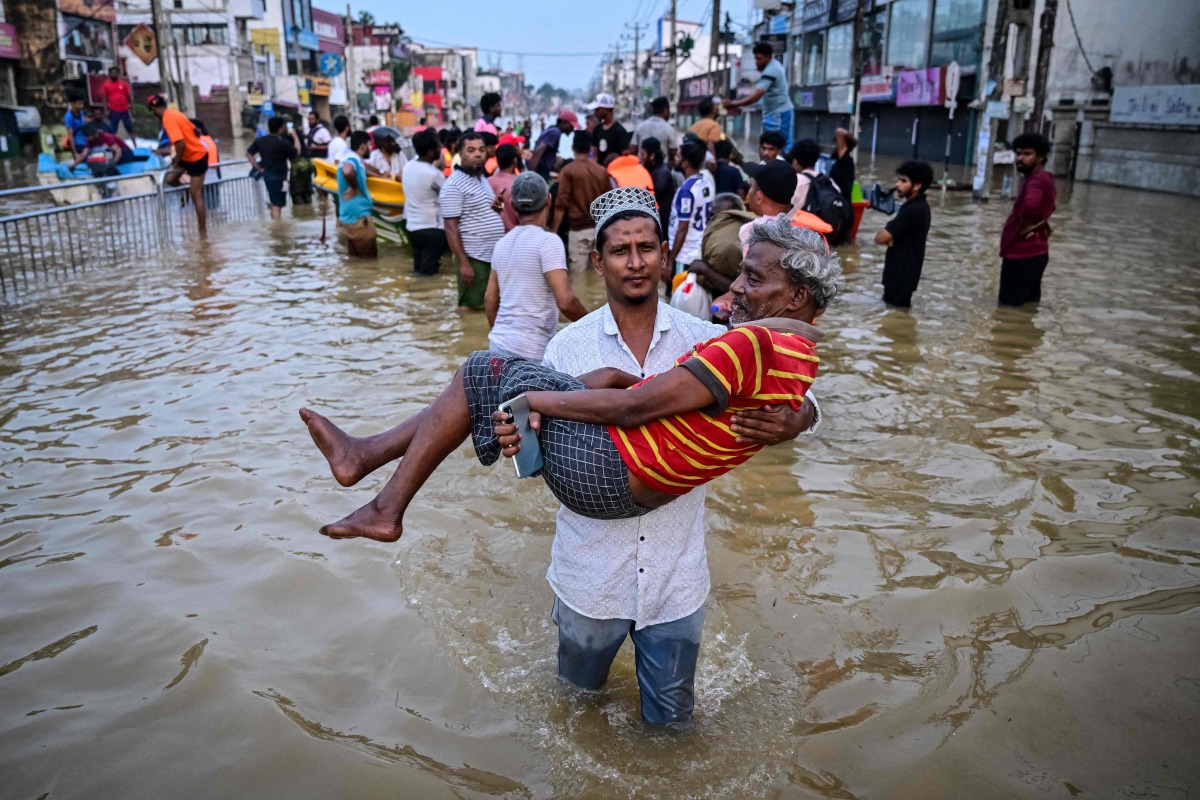 A youth carries an elderly man as they wade through a flooded street after heavy rainfall in Wellampitiya on the outskirts of Colombo on November 30, 2025. (Photo by Ishara S. KODIKARA / AFP)
