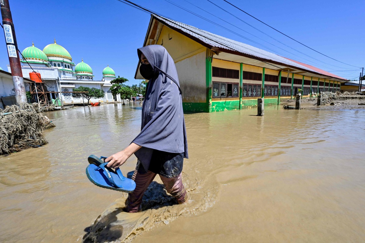 A woman walks past a mosque in a flooded area in Meureudu, Pidie Jaya district in Indonesia's Aceh province on November 30, 2025. (Photo by CHAIDEER MAHYUDDIN / AFP)
