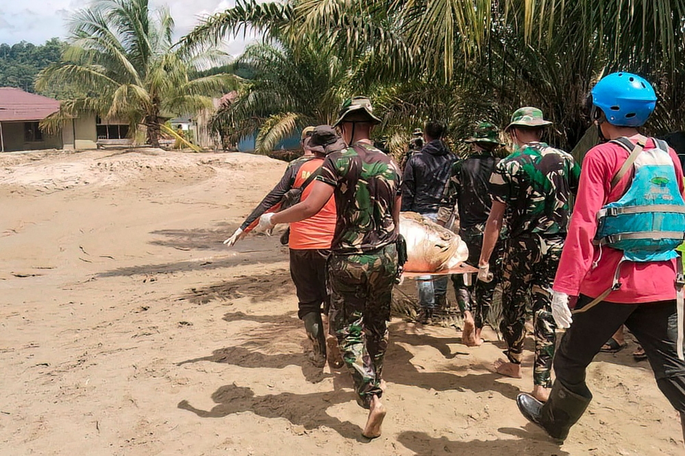 This handout image taken on November 30, 2025 and released on December 1, 2025 by Indonesia's National Search and Rescue Agency (Basarnas) shows military and rescue personnel carrying the body of a flood victim in Batangtoru, South Tapanuli, North Sumatra. (Photo by Handout / BASARNAS / AFP) 