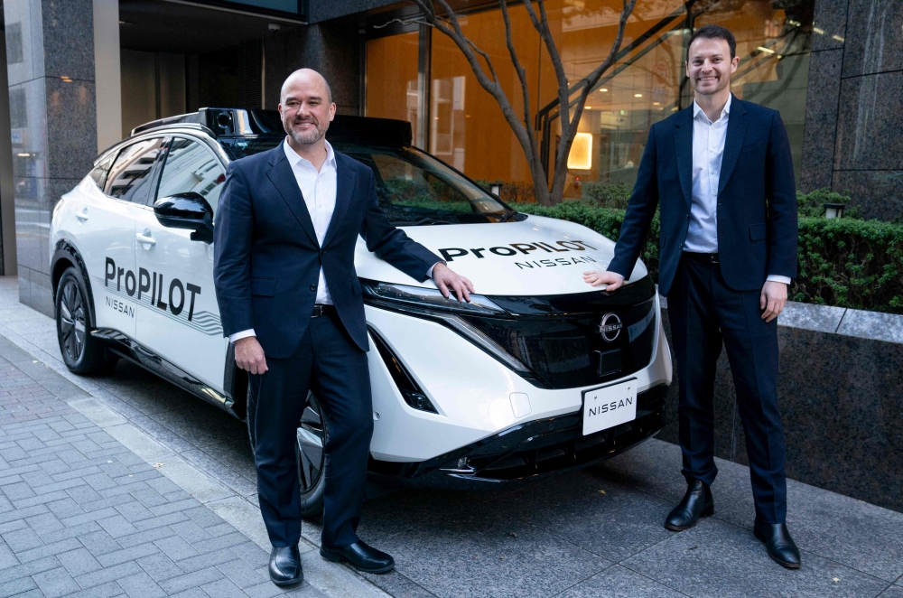 Nissan Motor CEO Ivan Espinosa (L) and Wayve Technologies CEO Alex Kendall (R) pose with a vehicle equipped with the ProPILOT next-generation driver assistance technology system after their signing ceremony in Tokyo on December 10, 2025. (Photo by Kazuhiro Nogi/ AFP)