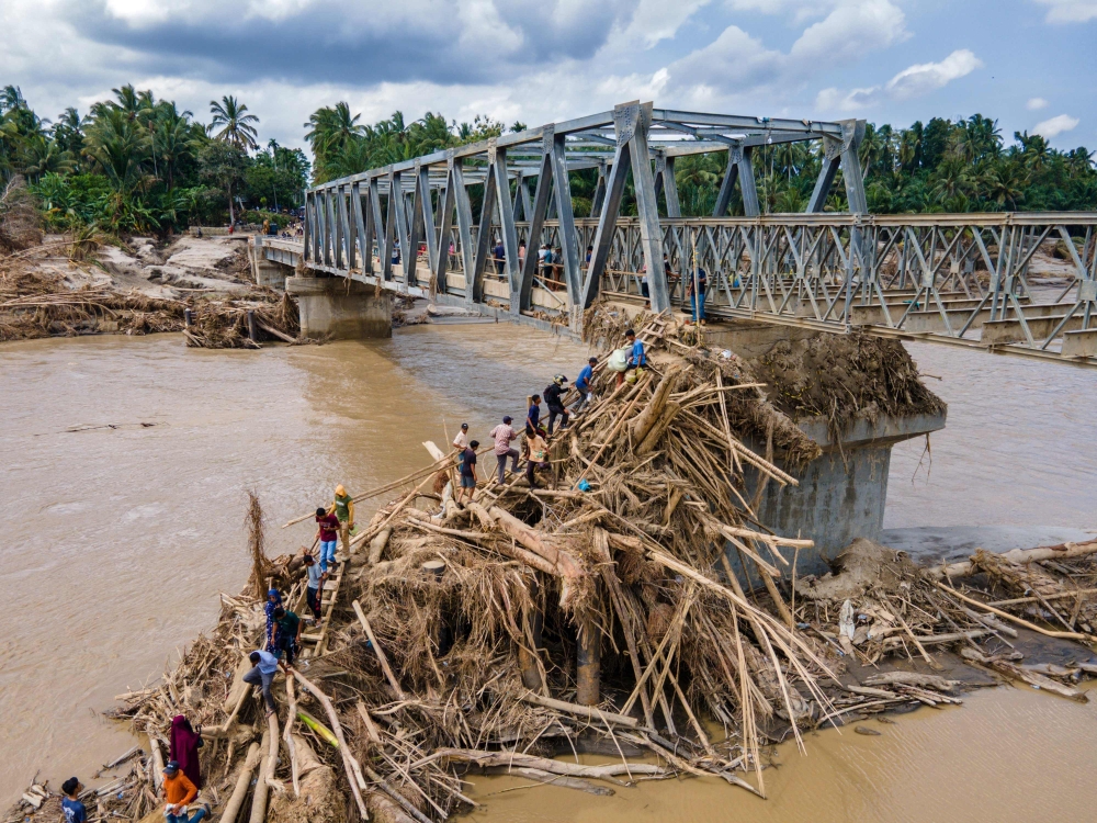 Aerial photo shows residents climbing debris to cross the river on a newly built bridge connecting Aceh and North Sumatra province on December 9, 2025. (Photo by Chaideer Mahyuddin / AFP)