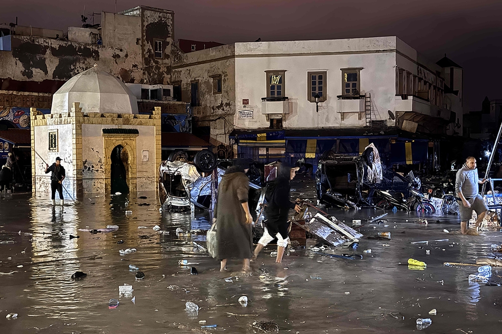 People wade through a square after a flash flood in Safi on December 14, 2025. Flash-flooding caused by sudden, heavy rain killed at least 21 people in the Moroccan coastal town of Safi on December 14, local authorities said. (Photo by AFP)