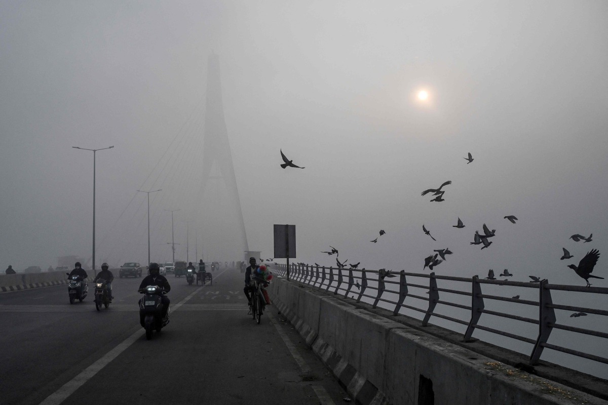 Commuters ride along the Signature Bridge over Yamuna river amid dense smog in NEW DELHI on December 27, 2025. (Photo by Arun SANKAR / AFP)
