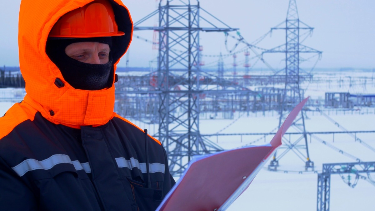 A worker at substation checking documents. Winter conditions highlight complexity and importance of maintaining power supply in cold weather.