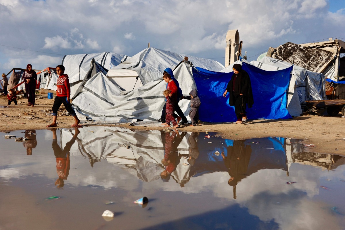 Displaced Palestinians walk past a large pool of rain water accumulated near tent shelters as the region experiences rain and cold winter conditions, in Gaza City on December 28, 2025. Photo by Omar AL-QATTAA / AFP