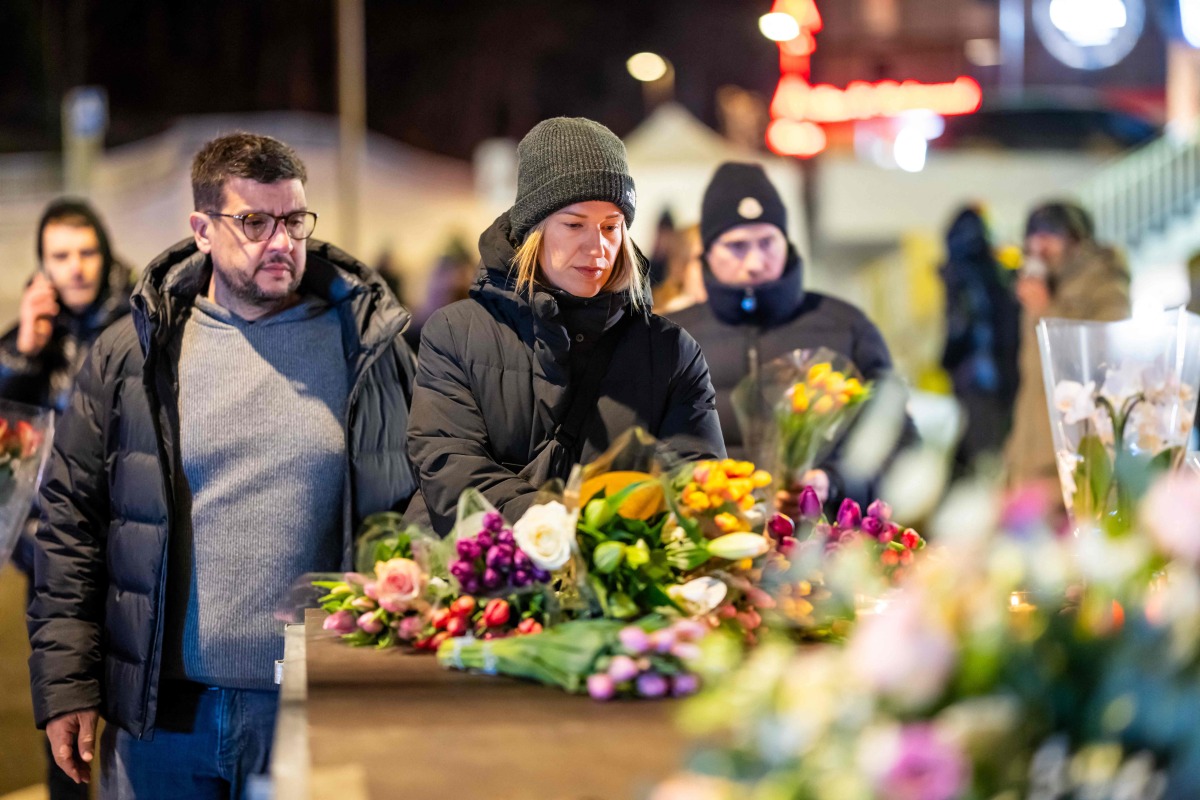 Mourners gather in front of flowers and candles laid near the site where a fire ripped through a crowded establishment during New Year's Eve celebrations in the Alpine ski resort town of Crans-Montana on January 1, 2026. Photo by MAXIME SCHMID / AFP