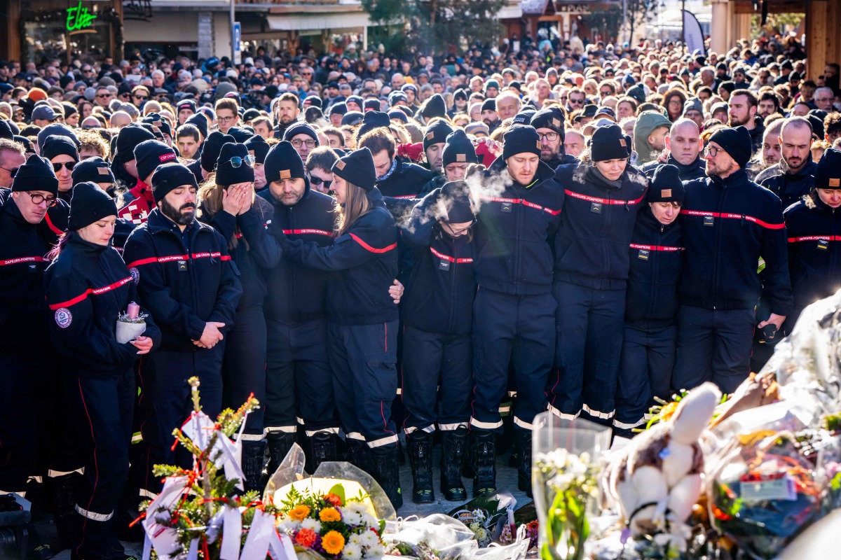 Firefighters from the Municipality of Crans-Montana react as they gather around a makeshift memorial to pay their respects by laying flowers, candles and messages near the Constellation, on January 4, 2026, in Crans-Montana in honour of the victims of the fire that ripped through the venue in the luxury Alpine ski resort on New Year's Eve. Photo by MAXIME SCHMID / AFP