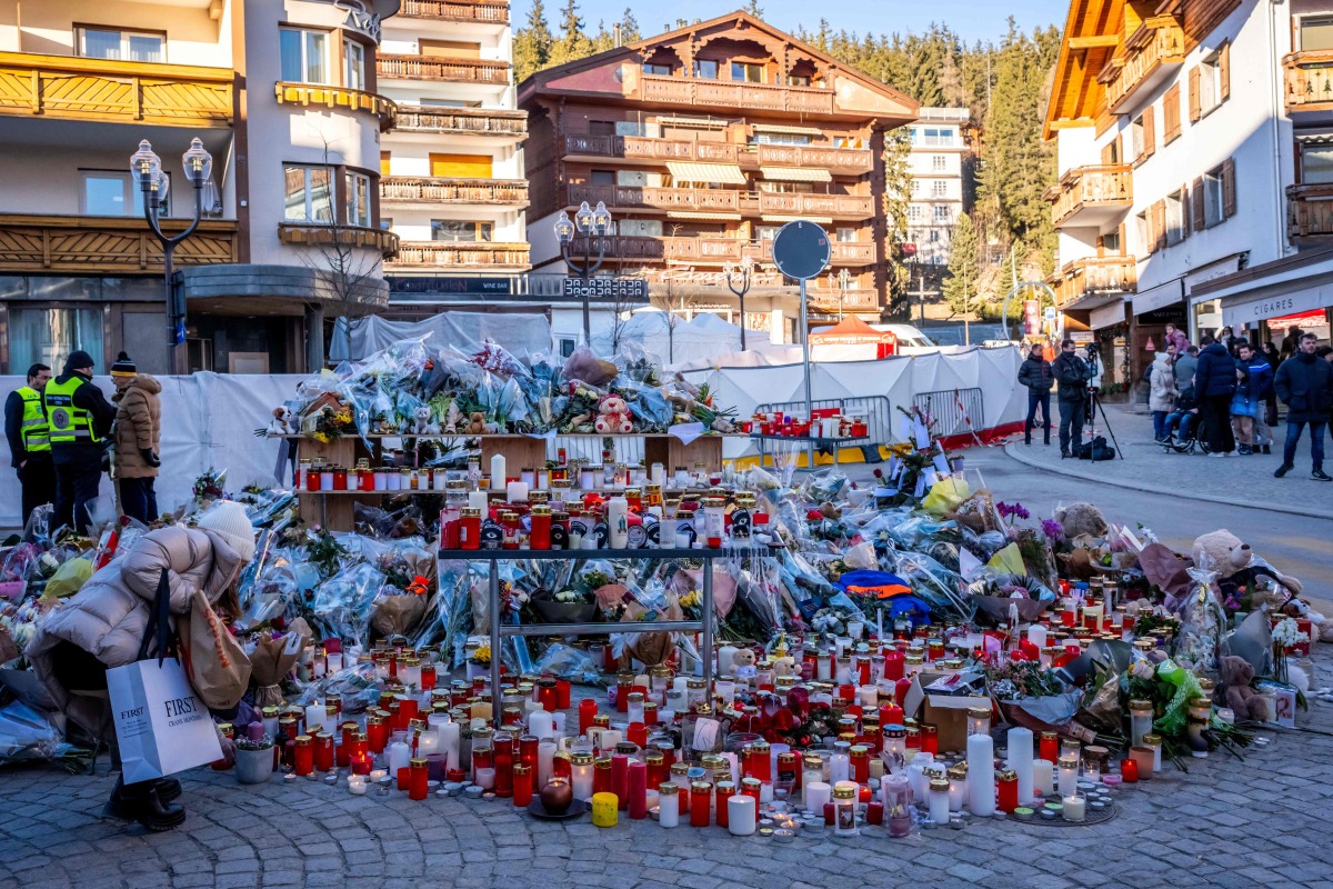 A mourner lays a flower bouquet at a makeshift memorial near the Constellation, on January 4, 2026, in Crans-Montana in honour of the victims of the fire that ripped through the venue in the luxury Alpine ski resort on New Year's Eve. Photo by MAXIME SCHMID / AFP