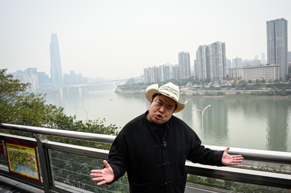 The photo taken on December 15, 2025 shows Donald Trump's impersonator Ryan Chen speaking as his assistant records a video along the Jialing River, in southwestern China's Chongqing municipality. (Photo by Jade Gao / AFP)