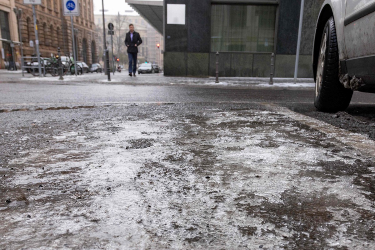 Melting ice is seen on the ground as a commuter makes his way in central Berlin, on January 13, 2026. Photo by Amelie HEIDUK / AFP