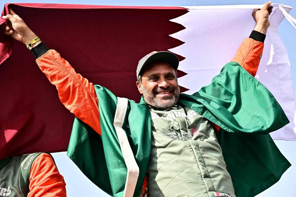 The Dacia Sandriders' Qatari driver Nasser al-Attiyah holds Qatar's flag while celebrating his win in the 48th edition of the Dakar Rally 2026 in Yanbu, Saudi Arabia. (Photo by Giuseppe Cacace / AFP)
 