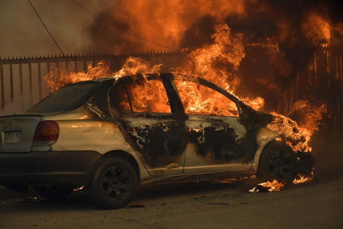 A vehicle and a house are engulfed in flames during a wildfire in Concepcion, Chile, on January 18, 2026. Photo by GUILLERMO SALGADO / AFP
