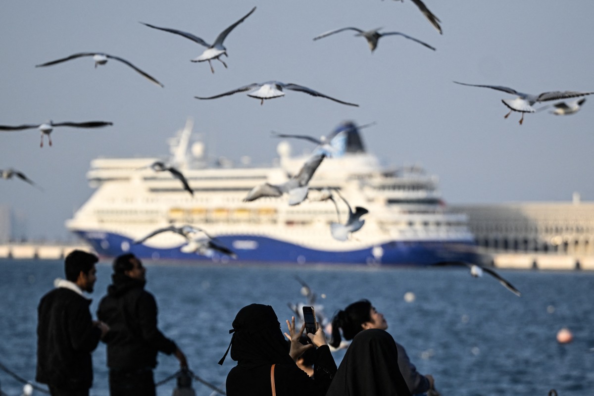 A woman uses her mobile phone to take pictures of the seagulls at the old seaport in Doha on January 20, 2026. (Photo by MAHMUD HAMS / AFP)
