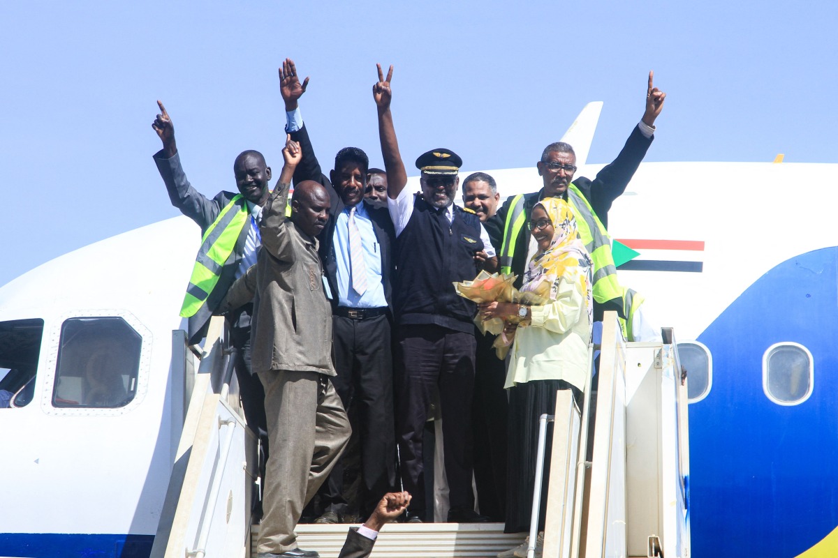 Sudan Airways members of staff celebrate as they stand at the door of the first domestic flight arriving from Port Sudan, after it landed at Khartoum International Airport following a three-year hiatus, on February 1, 2026. (Photo by Ebrahim Hamid / AFP)