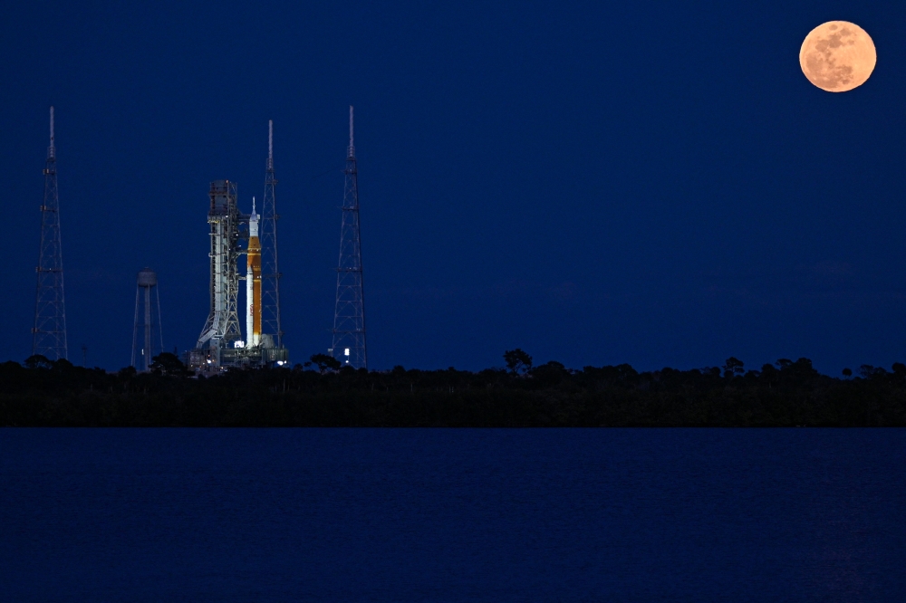 A full moon rises as the Space Launch System (SLS) rocket and the Orion spacecraft, integrated for the Artemis II mission, are seen at the Kennedy Space Center, on February 1, 2026. (Photo by Miguel J. Rodriguez Carrillo / AFP)
 