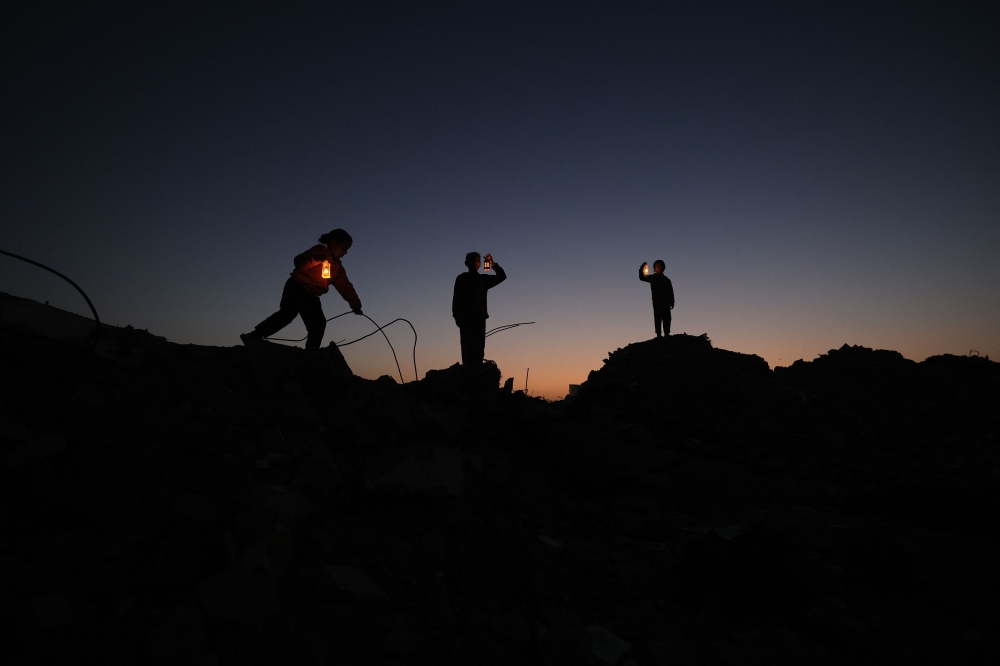 Young displaced Palestinians play on the ruins of destroyed buildings, carrying Ramadan lanterns, in central Gaza Strip on February 15, 2026. (Photo by Eyad Baba / AFP)
 