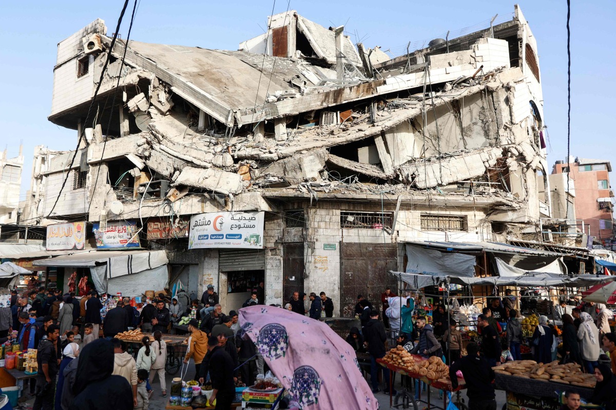 Palestinians shop for food beneath a destroyed building in Gaza City's Zawiya market on February 18, 2026, on the first days of the holy fasting month of Ramadan. (Photo by Omar AL-QATTAA / AFP)
