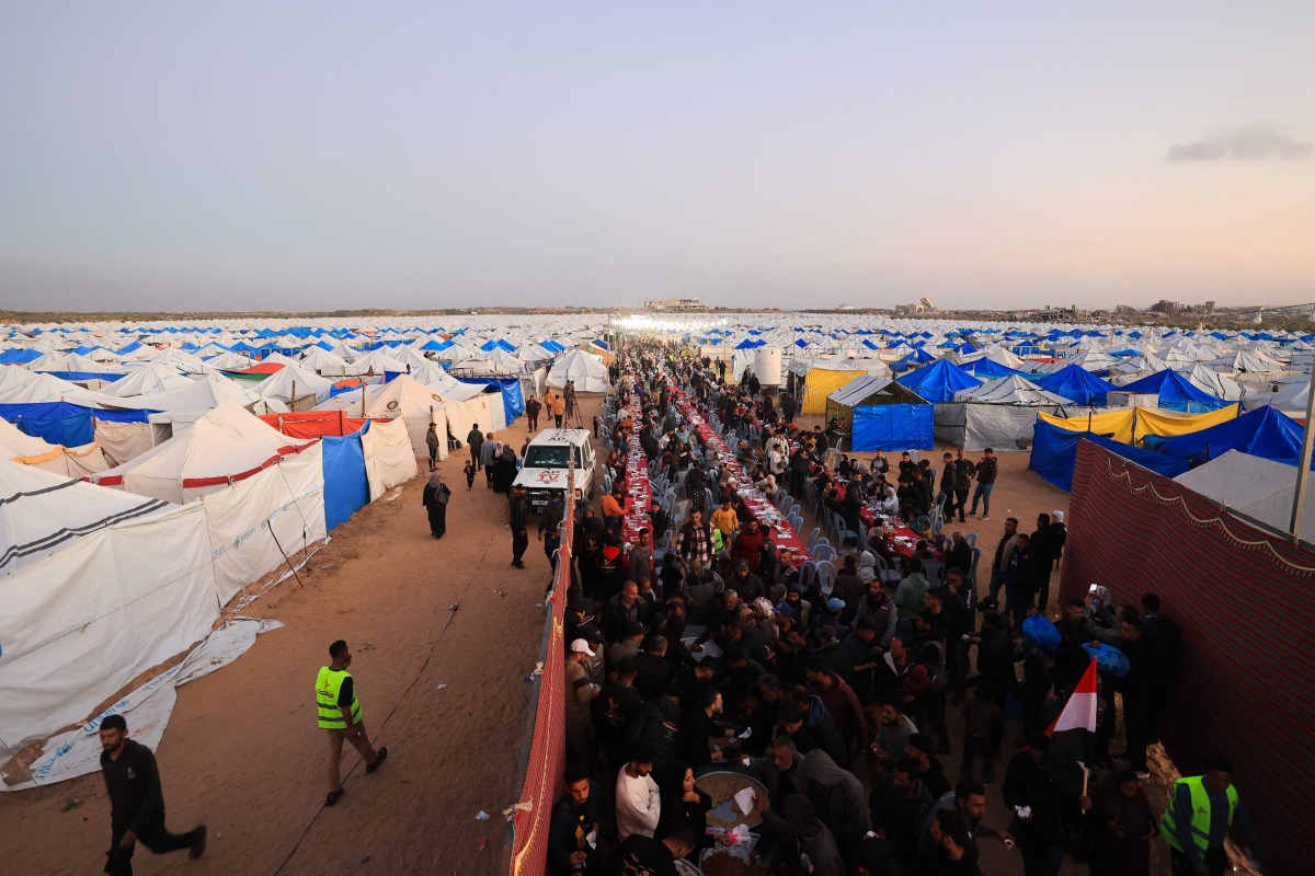 Displaced Palestinian families sit at communal long tables as they gather to break the dawn-to-dusk Ramadan fast during Iftar, in the al-Zahara neighborhood, north of the Nuseirat refugee camp in the central of Gaza Strip on February 21, 2026. (Photo by Eyad Baba / AFP)
