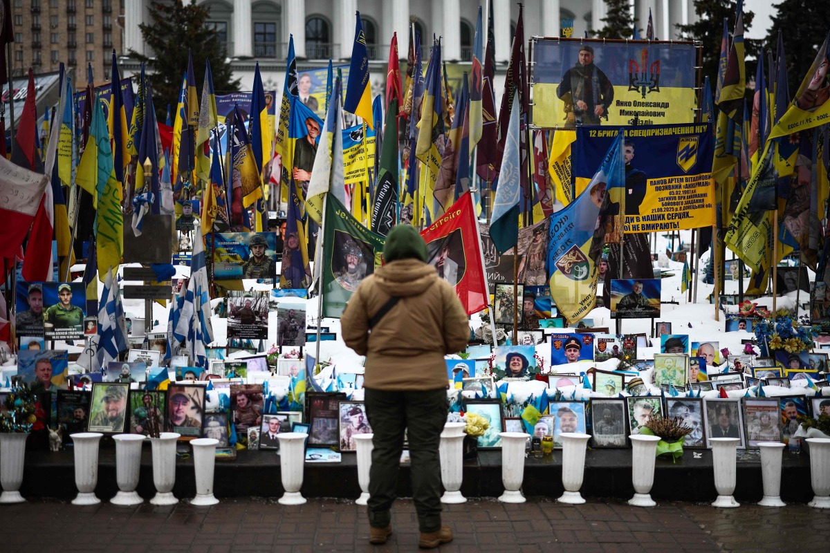 A person stands at a makeshift memorial to fallen Ukrainian and foreign soldiers in Independence Square in Kyiv on February 23, 2026. (Photo by HENRY NICHOLLS / AFP)