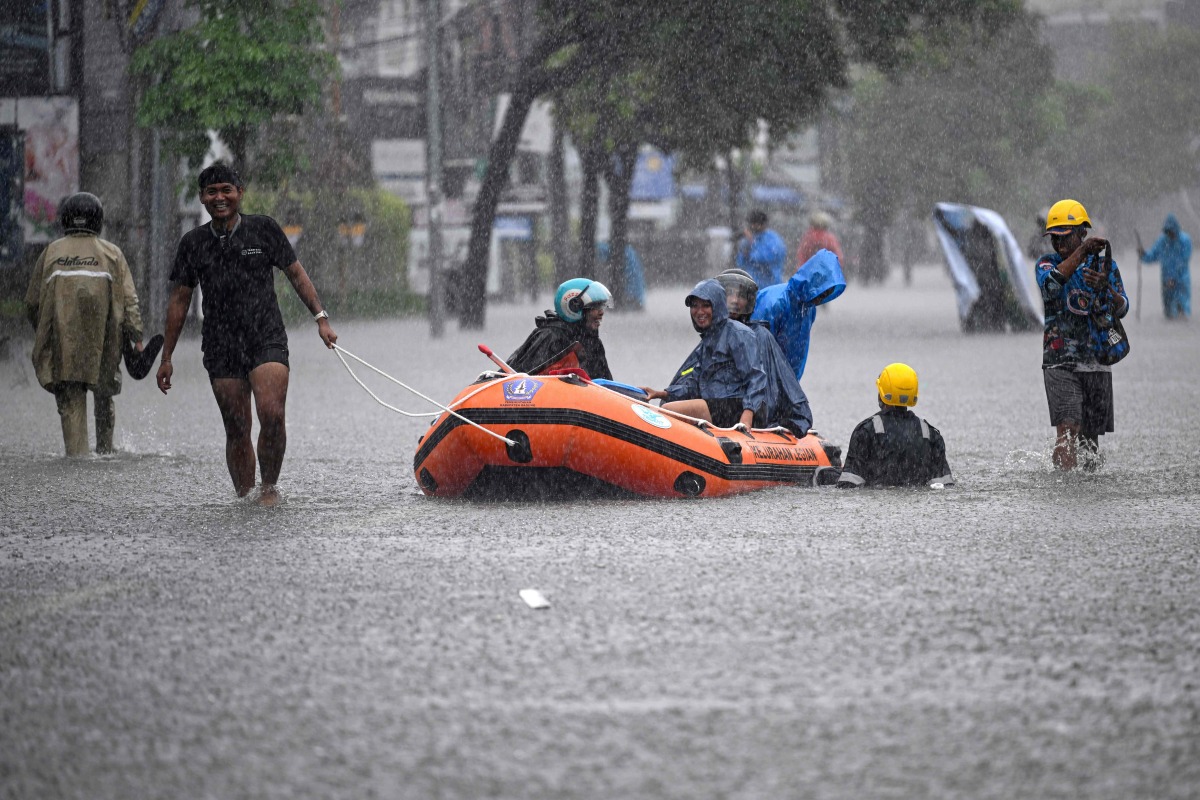 Local residents move hotel guests using a rubber boat through the water on an inundated street amid floods following heavy rain at Legian Kuta near Denpasar on Indonesia's resort island of Bali on February 24, 2026. (Photo by SONNY TUMBELAKA / AFP)