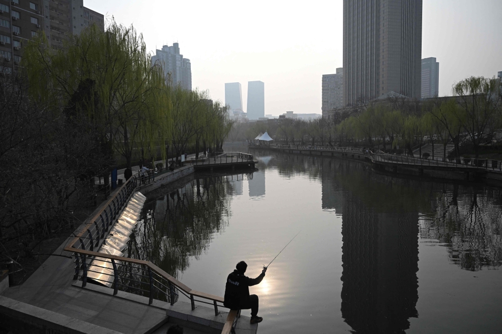 An angler fishes by the Liangma River on a spring day in Beijing on March 24, 2026. (Photo by Pedro Pardo / AFP)
 