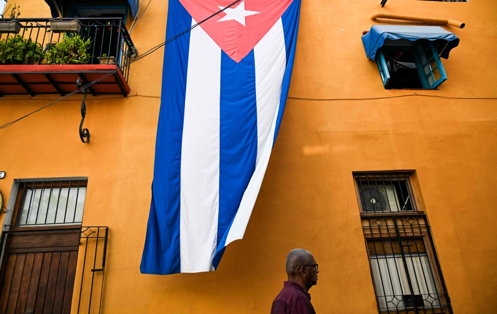 A man walks past a Cuban flag hanged on the facade of a house in Havana on March 26, 2026. (Photo by Yamil Lage / AFP)