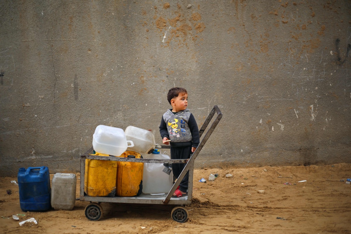 A displaced Palestinian boy stands on a trolley loaded with empty water canisters at the Nuseirat refugee camp, in the central Gaza Strip on April 1, 2026. (Photo by Eyad Baba / AFP)
