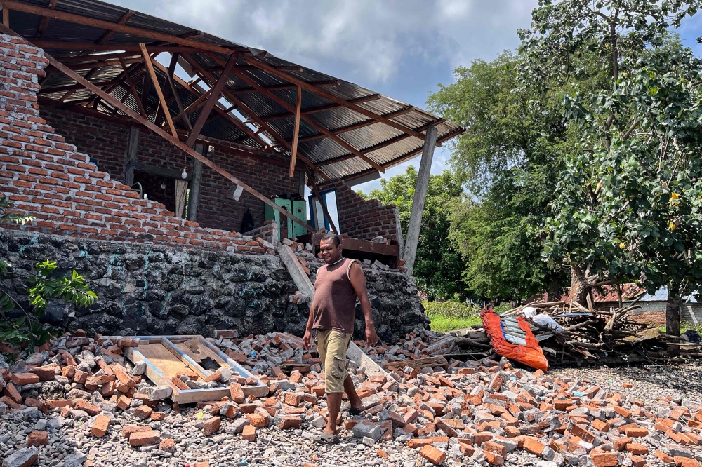 A resident clears debris from a damaged wall of his home after a shallow 4.9 magnitude earthquake in Adonara, East Nusa Tenggara on April 9, 2026, damaging dozens of homes and injuring multiple people, an official said. (Photo by Handrianus Hali / AFP)