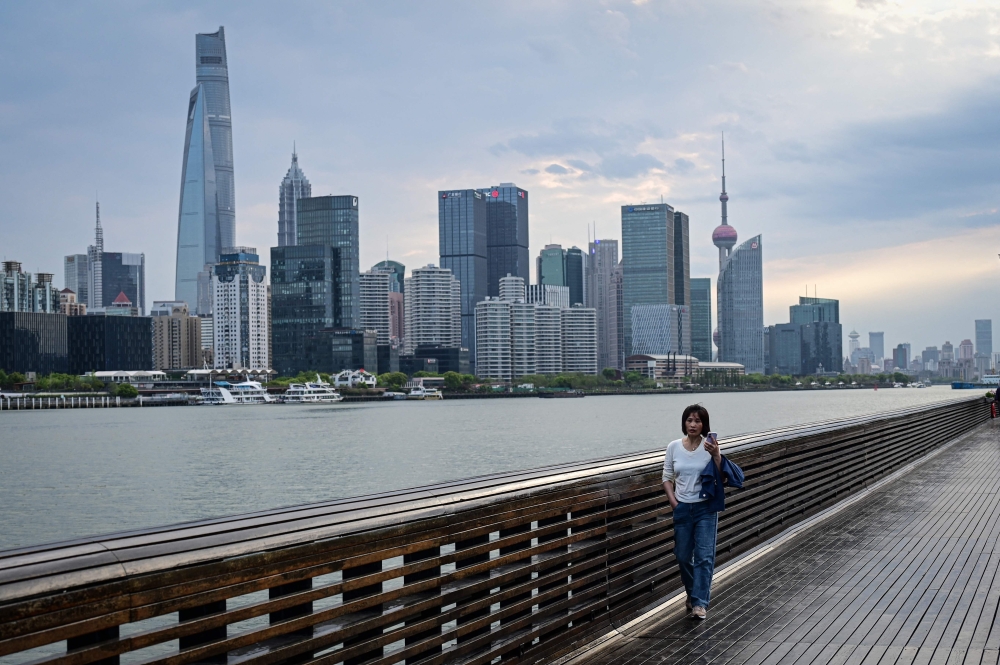 A woman walks along the Huangpu River as the city's skyline is seen in the background in Shanghai on April 9, 2026. (Photo by Jade Gao / AFP)