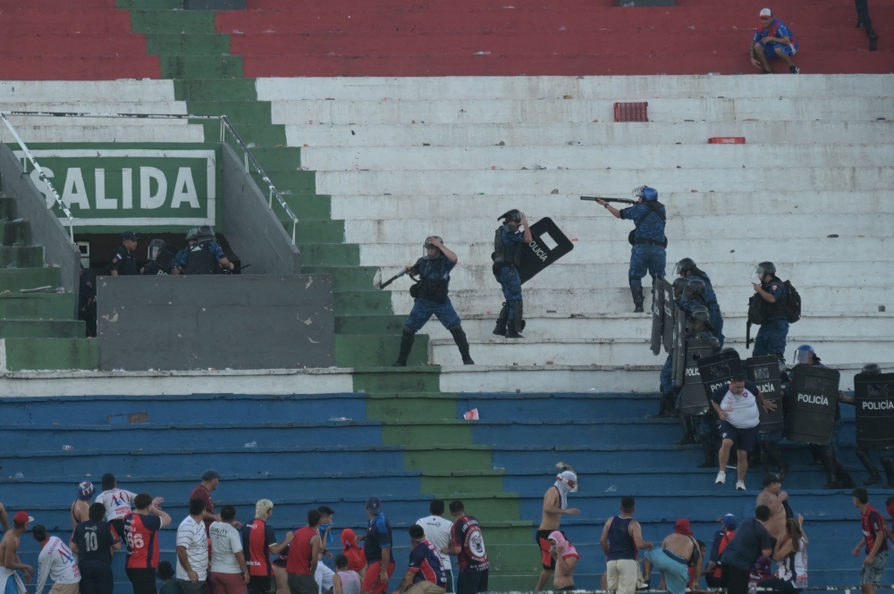 Fans of Cerro Porteno clash with police officers during the Paraguayan tournament football match between Olimpia and Cerro Porteno at the Defensores del Chaco stadium in Asuncion on April 19, 2026. (Photo by Daniel Duarte / AFP)