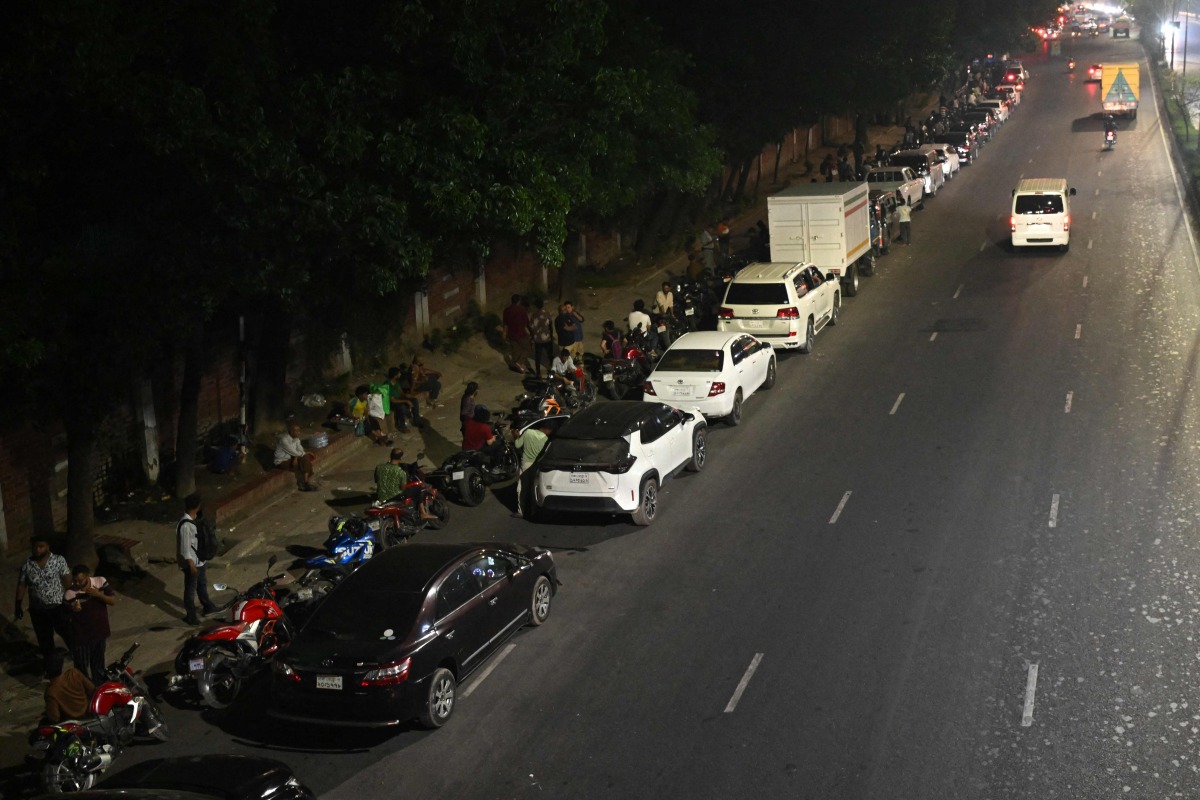 People queue up along a road, to refuel their vehicles at a filling station in Dhaka on April 21, 2026. (Photo by MUNIR UZ ZAMAN / AFP)