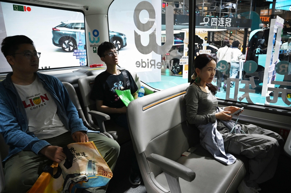 Visitors try out a WeRide autonomous vehicle at the Beijing Auto Show in Beijing on April 26, 2026. (Photo by Greg Baker / AFP)