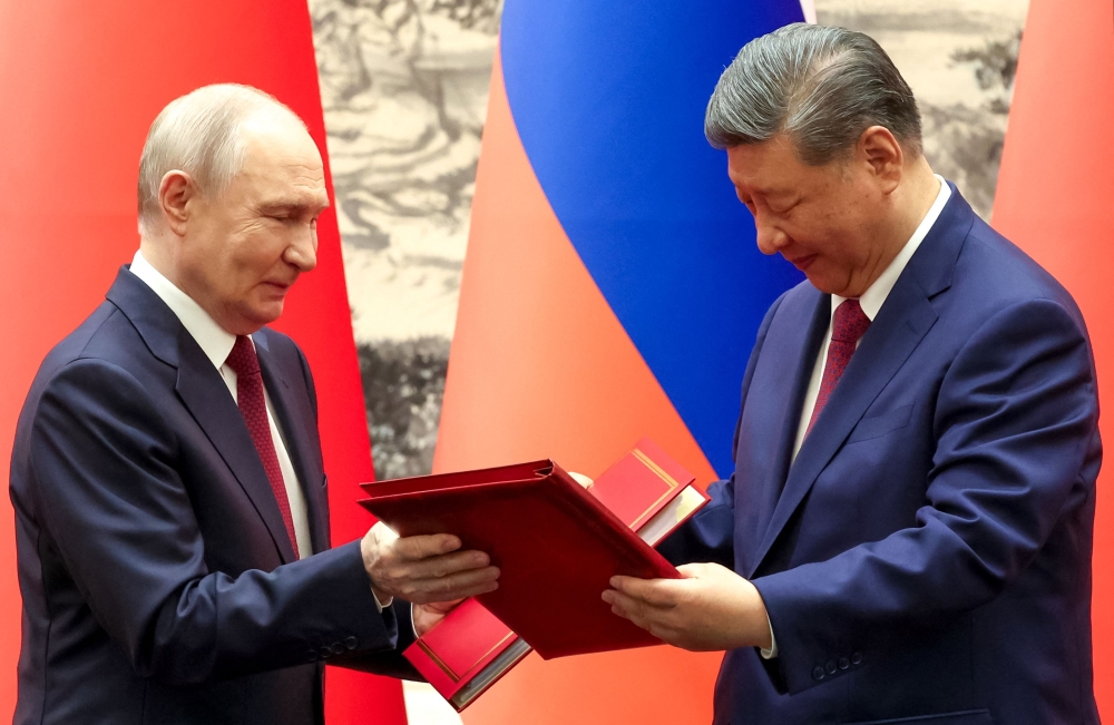 In this pool photograph distributed by the Russian state agency Sputnik, Russia's President Vladimir Putin and China's President Xi Jinping exchange documents during a signing ceremony following their talks in Beijing on May 20, 2026. (Photo by Alexander Kazakov / POOL / AFP)