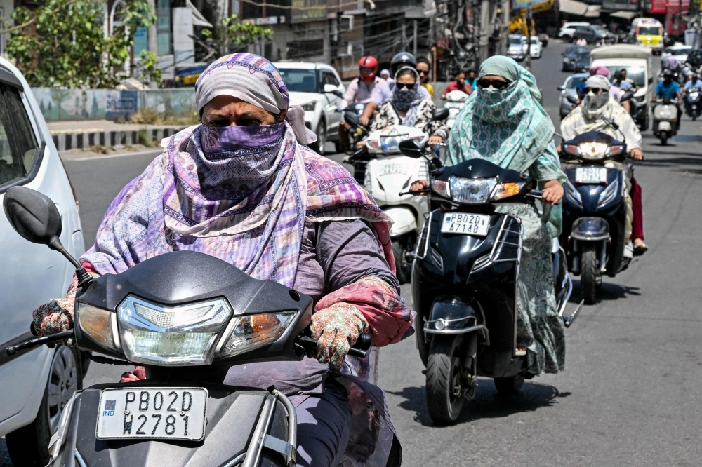 Commuters with their faces covered with cloth ride along a street on a hot summer afternoon in Amritsar on May 23, 2026. (Photo by Narinder NANU / AFP)
 