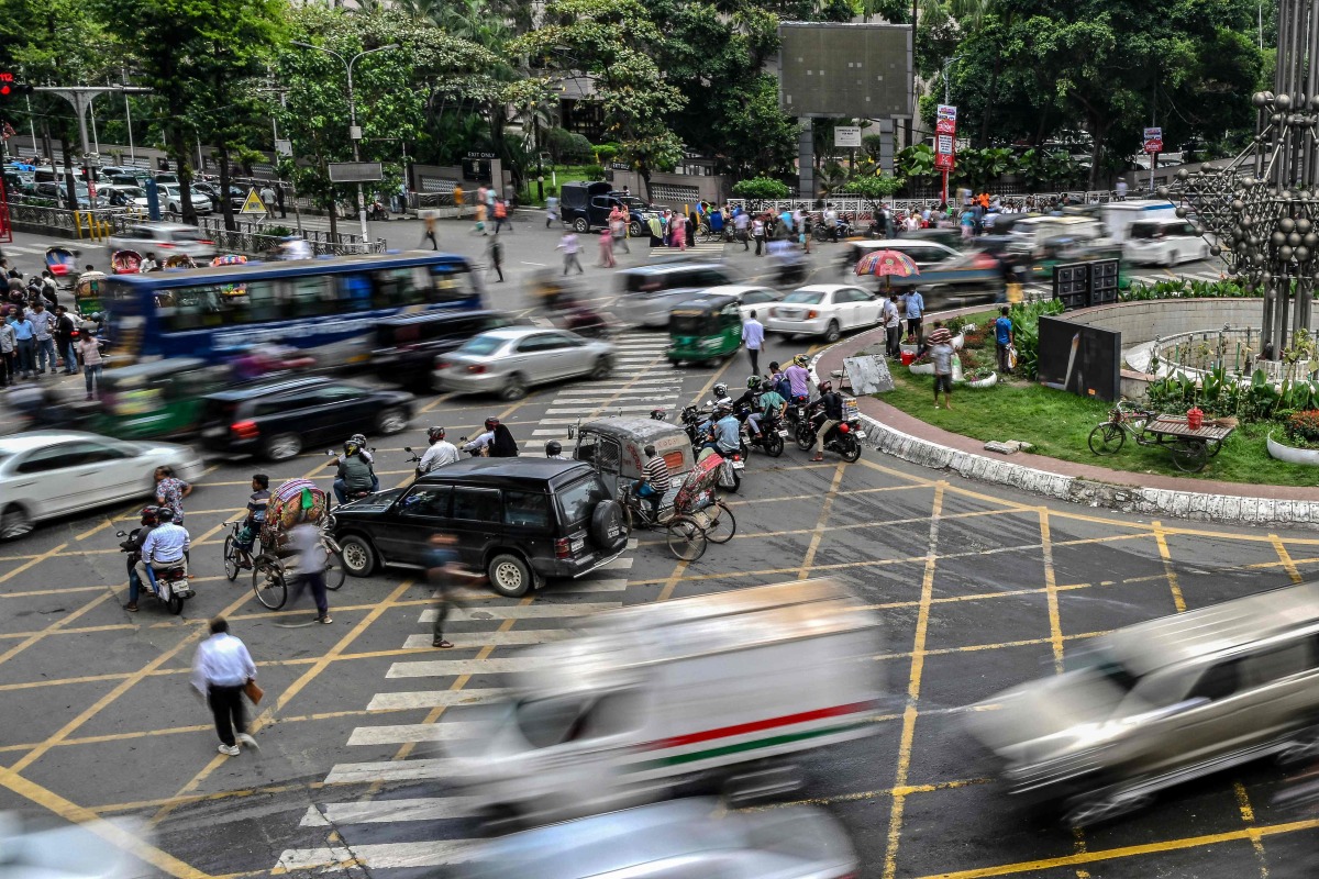 This photograph taken on May 14, 2026 shows commuters waiting to cross a road amid traffic in Dhaka. Photo by Munir UZ ZAMAN / AFP